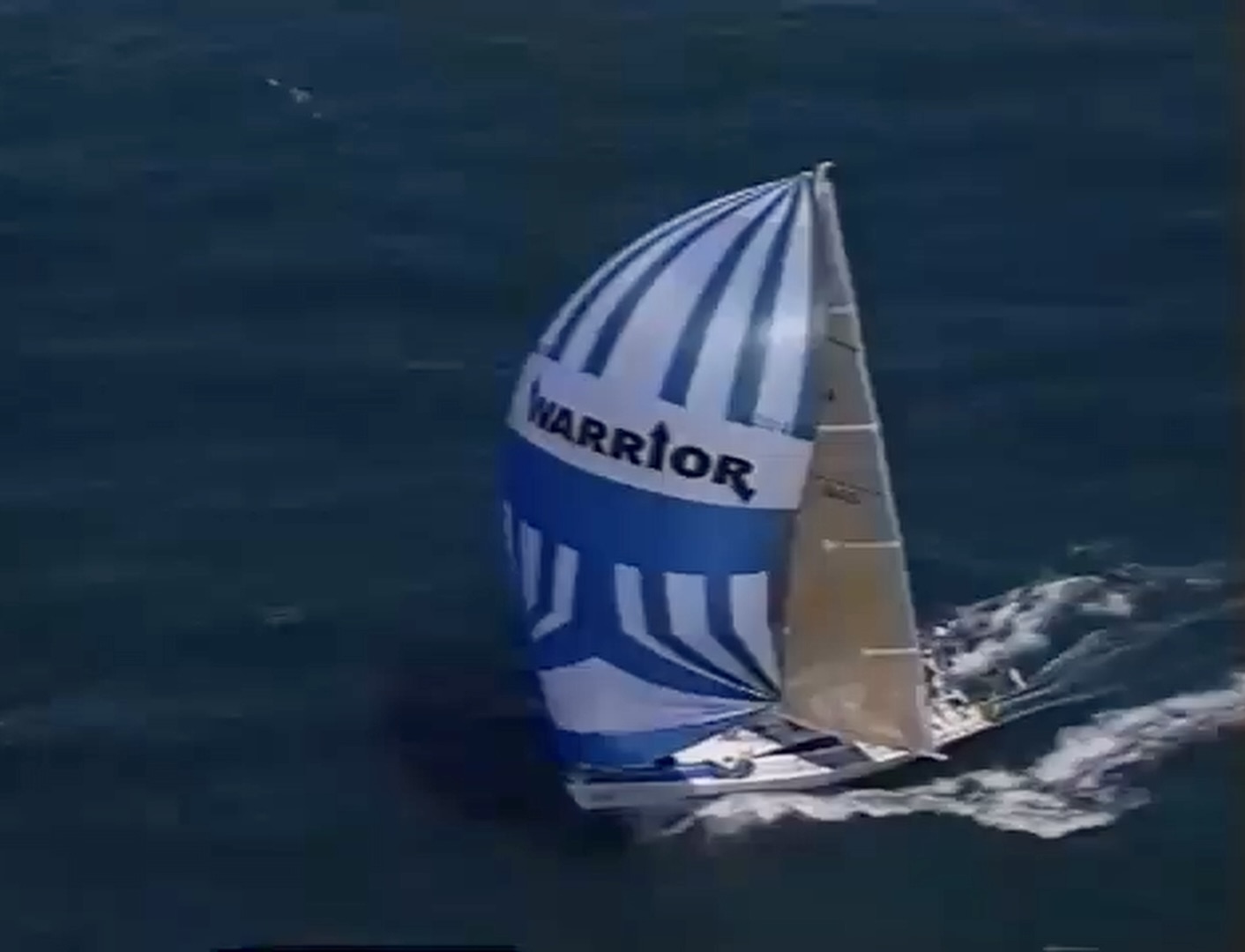 Warrior under a red and white spinnaker at dusk