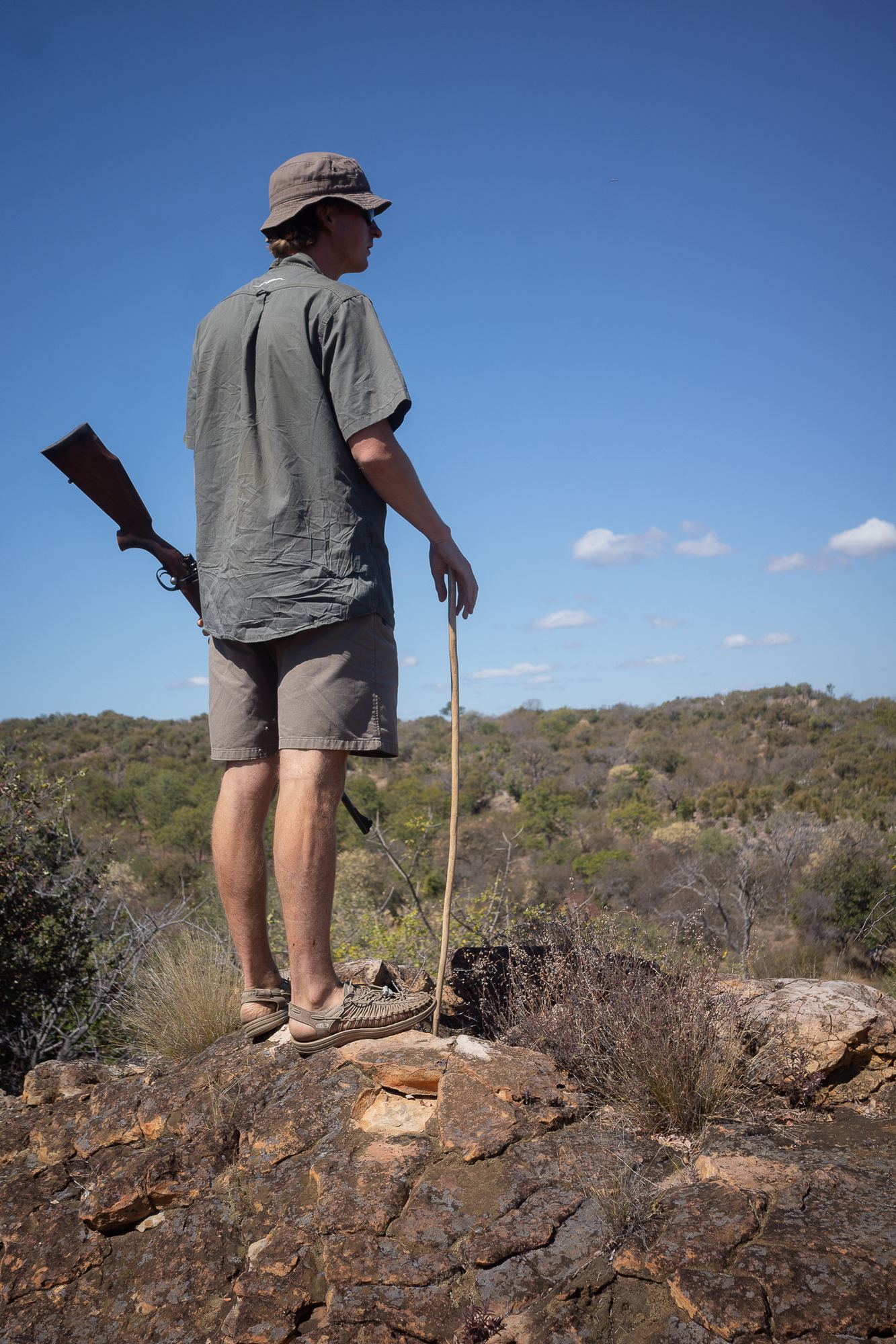 A guide with a rifle scanning from a rocky lookout