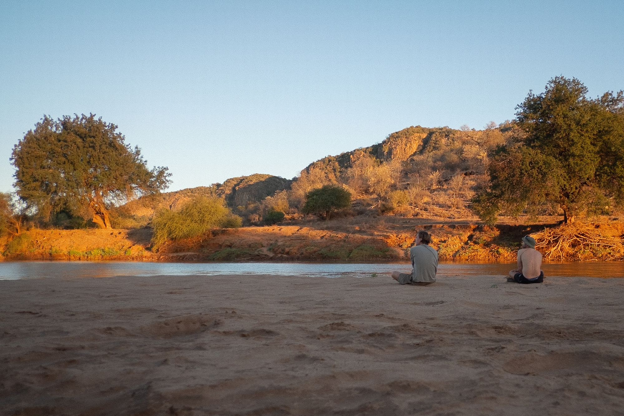 Two walkers resting on a riverbank at sundown